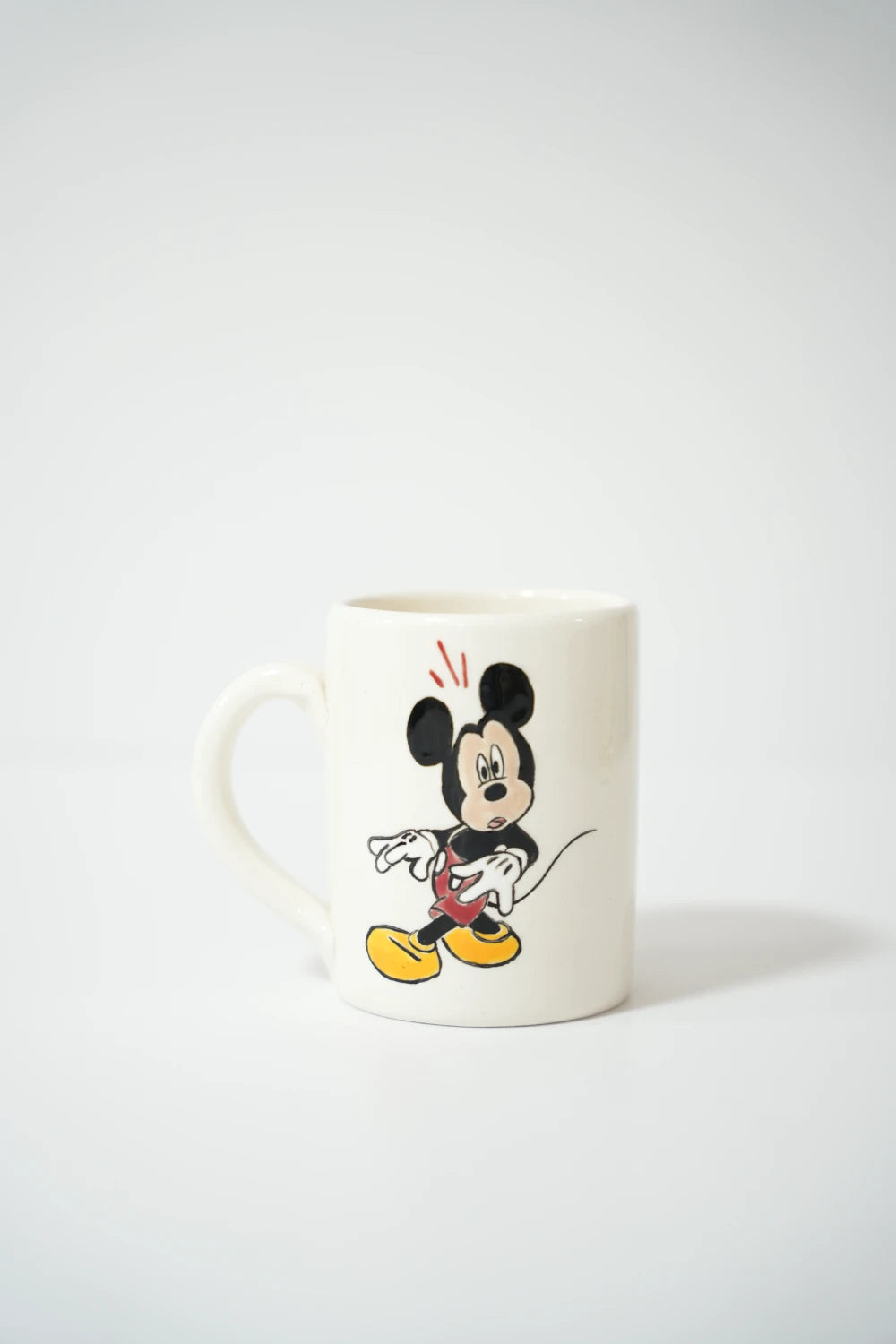 فنجان سيراميك أبيض مع رسمة شخصية كرتونية Mickey Mouse بألوان كلاسيكية.