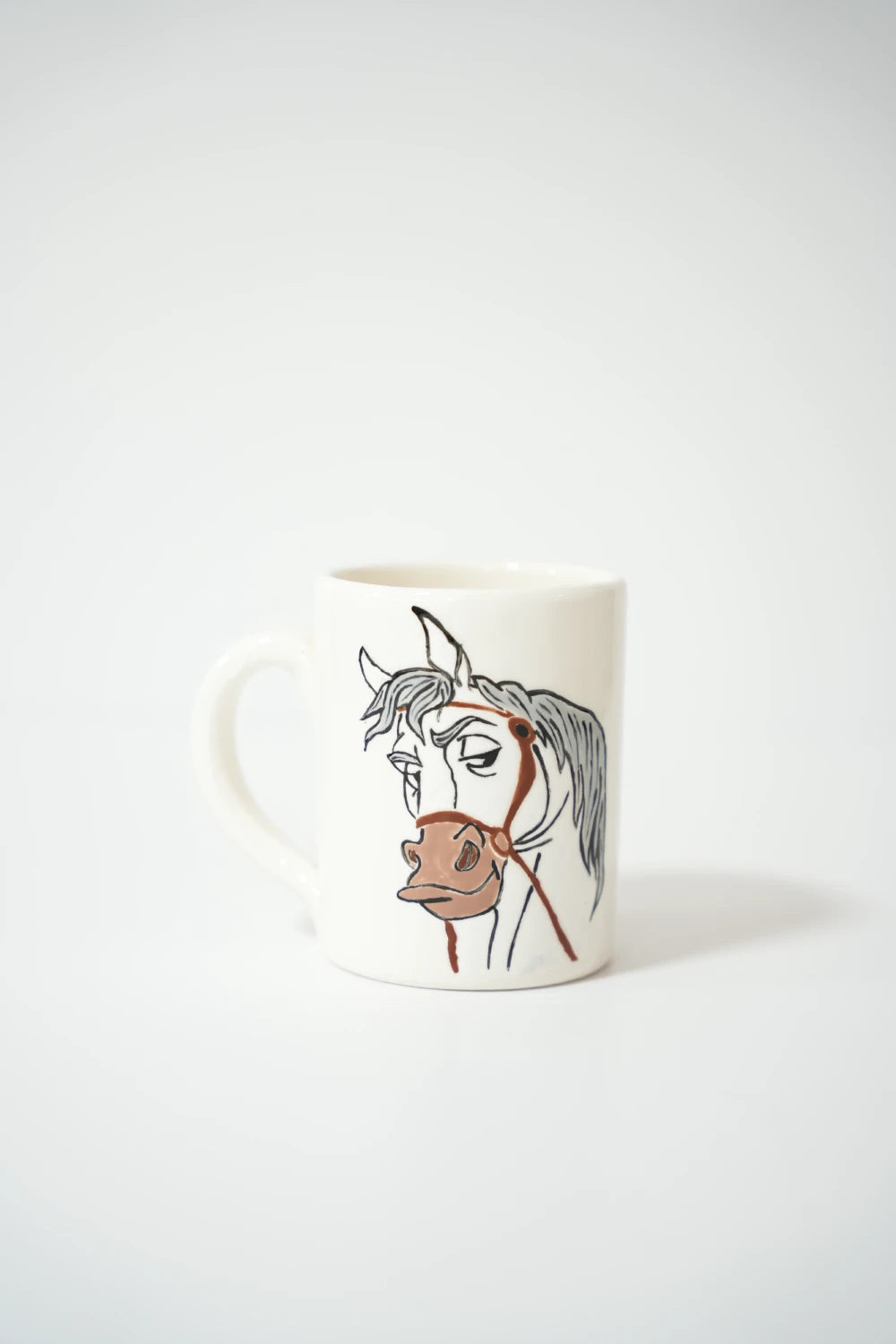 فنجان سيراميك أبيض مع رسمة حصان بتفاصيل خطوط بسيطة وأنيقة.