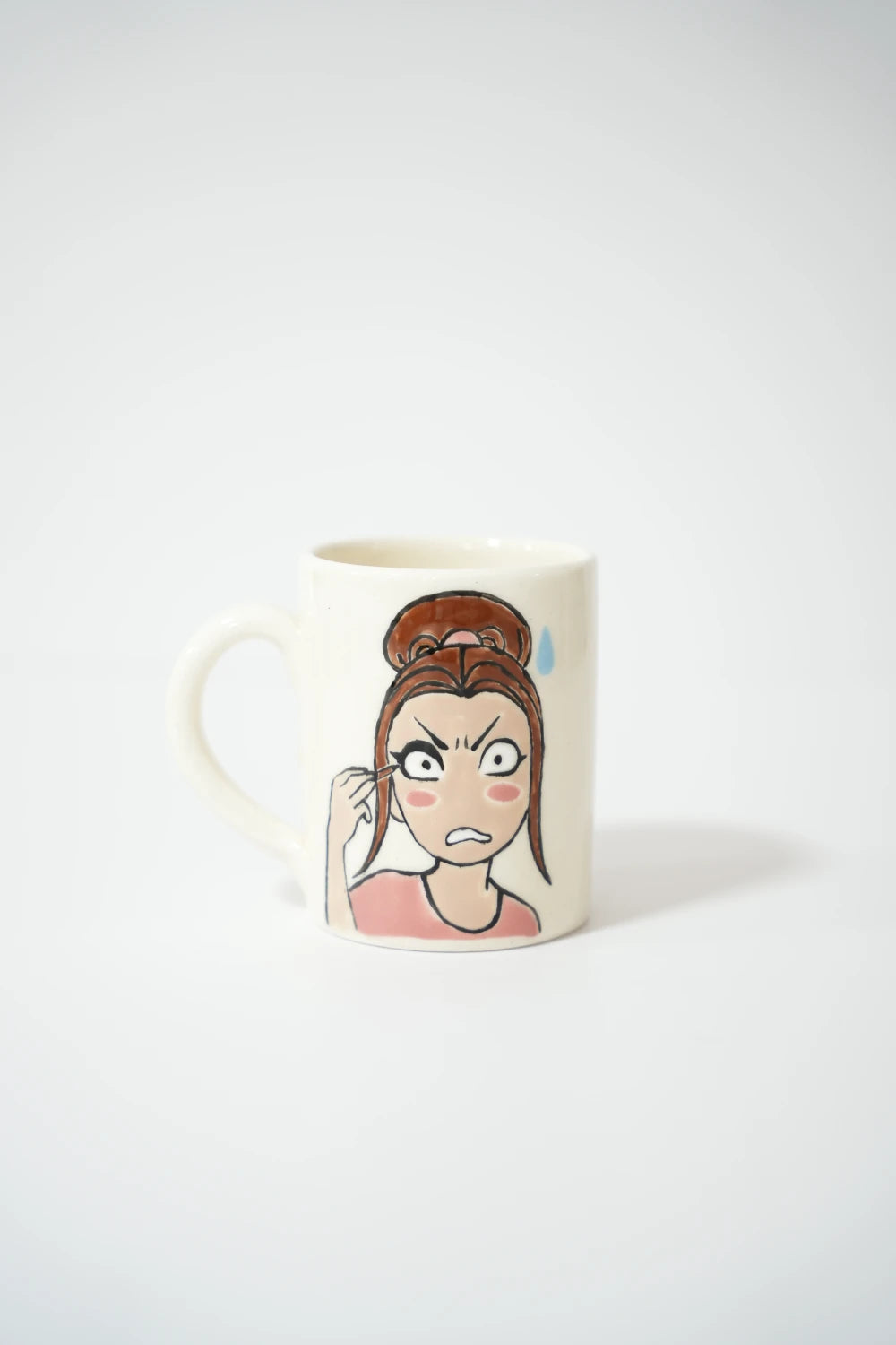 فنجان سيراميك أبيض مع رسمة بنت كرتونية بتعبير غاضب/منفعل.