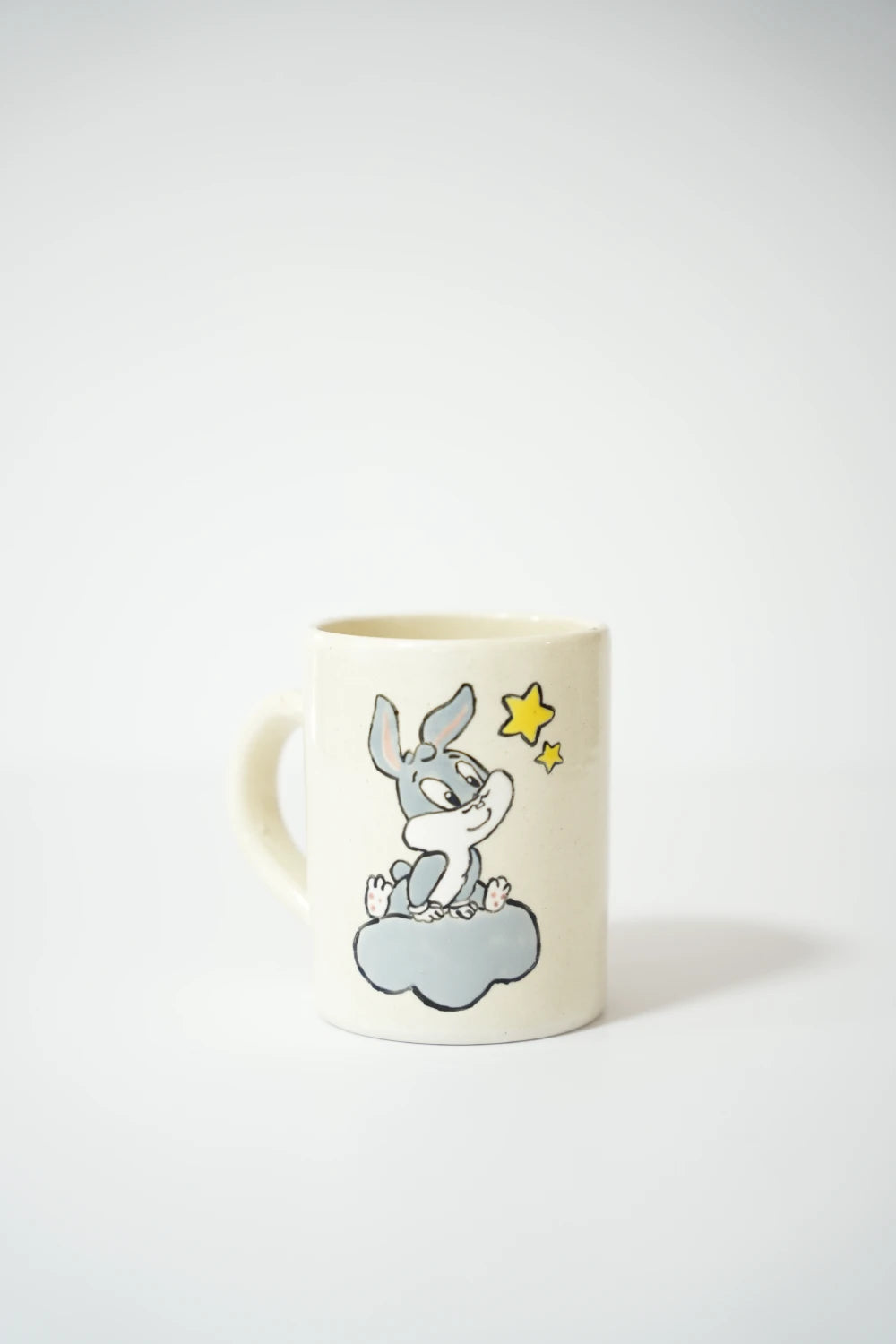 فنجان سيراميك أبيض مع رسمة Bugs Bunny جالس على غيمة مع نجوم صفراء.