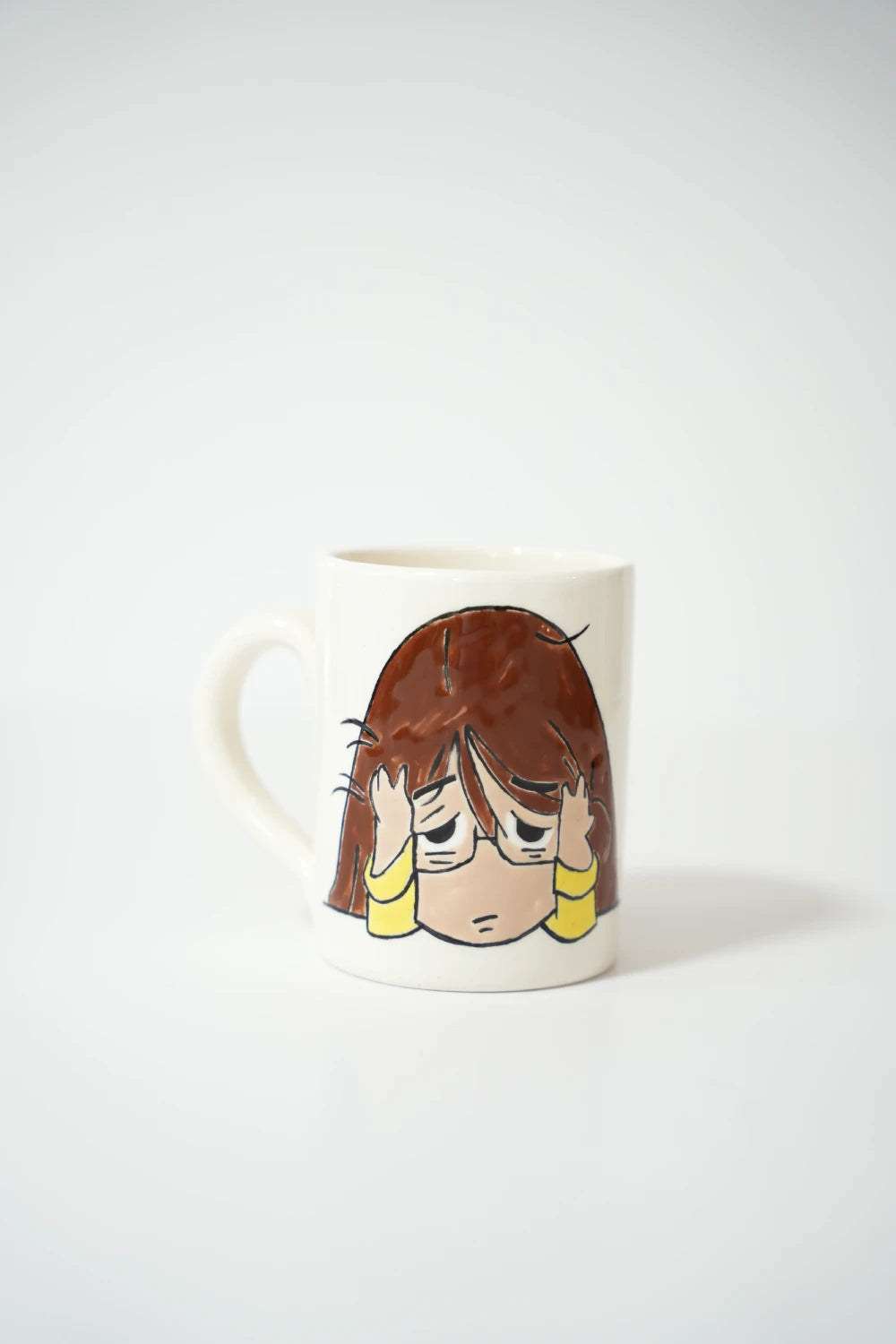 فنجان سيراميك أبيض مع رسمة بنت كرتونية مرهقة تضع يديها على رأسها.