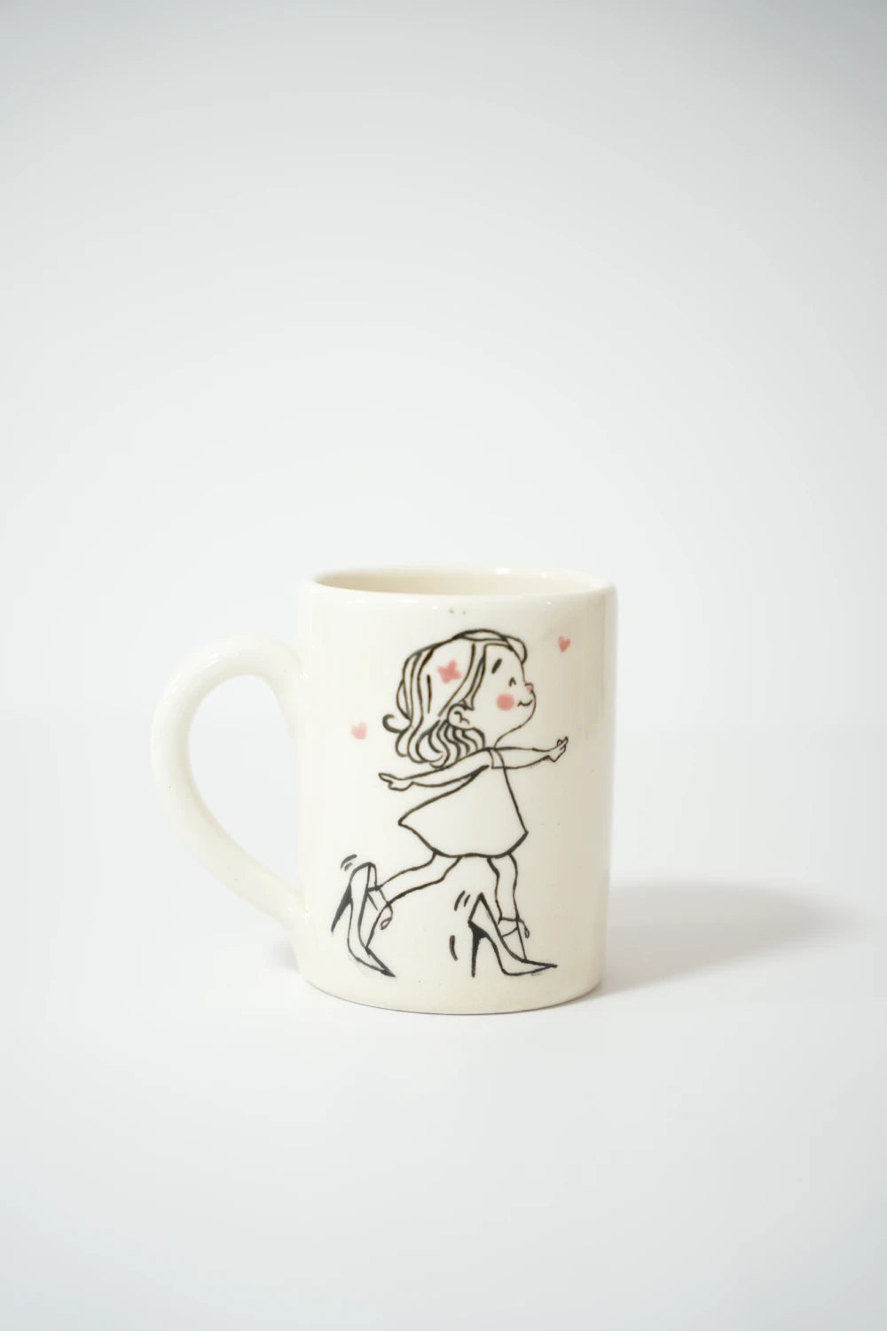 فنجان سيراميك أبيض مع رسمة بنت كرتونية تمشي بثقة وهي ترتدي كعب عالي.