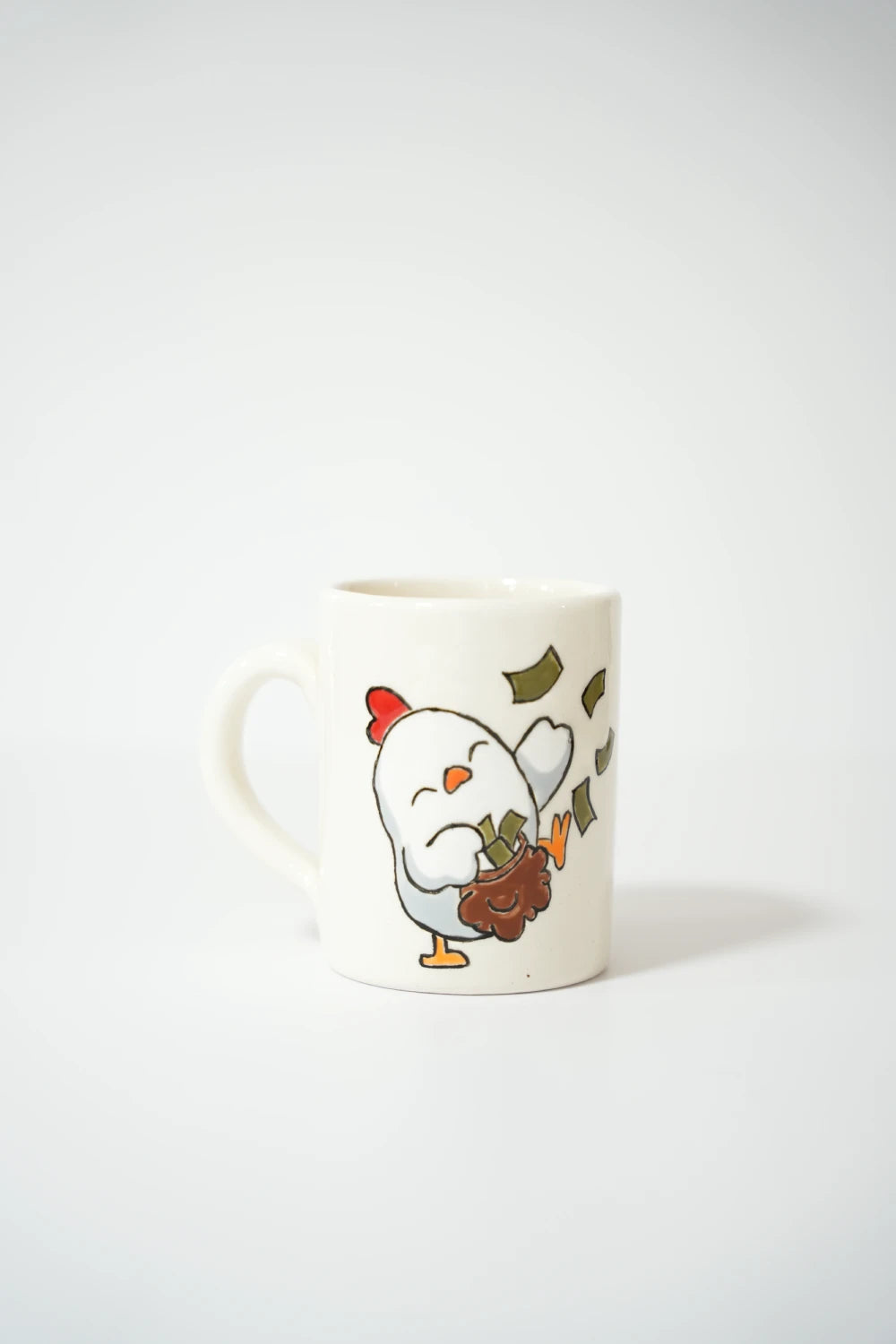 فنجان سيراميك أبيض عليه رسمة دجاجة كرتونية ترمي أوراق مال بطريقة طريفة.