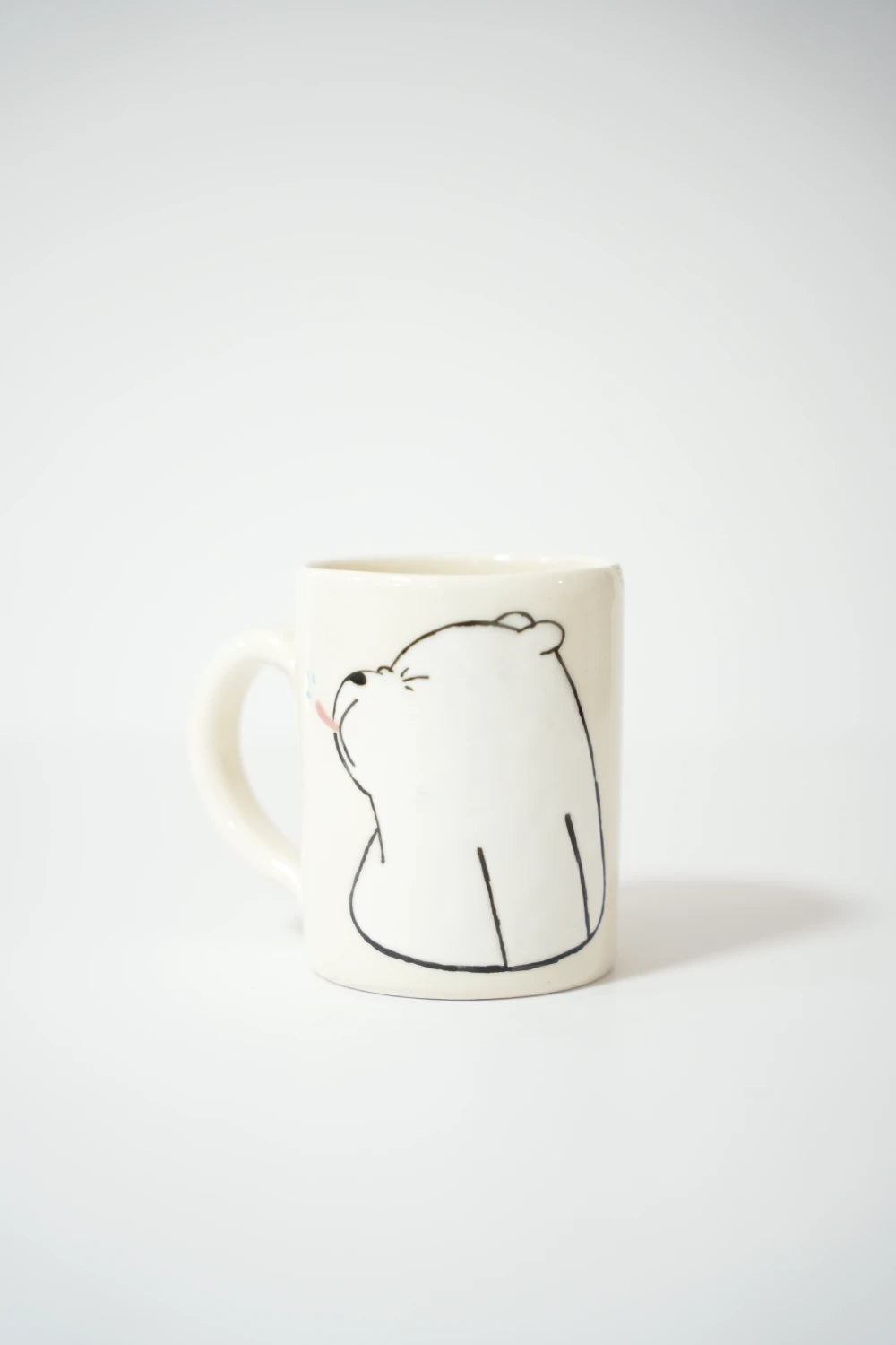 فنجان سيراميك أبيض مع رسمة دب كرتوني بتعبير منزعج مرسوم بخط أسود بسيط على خلفية بيضاء.