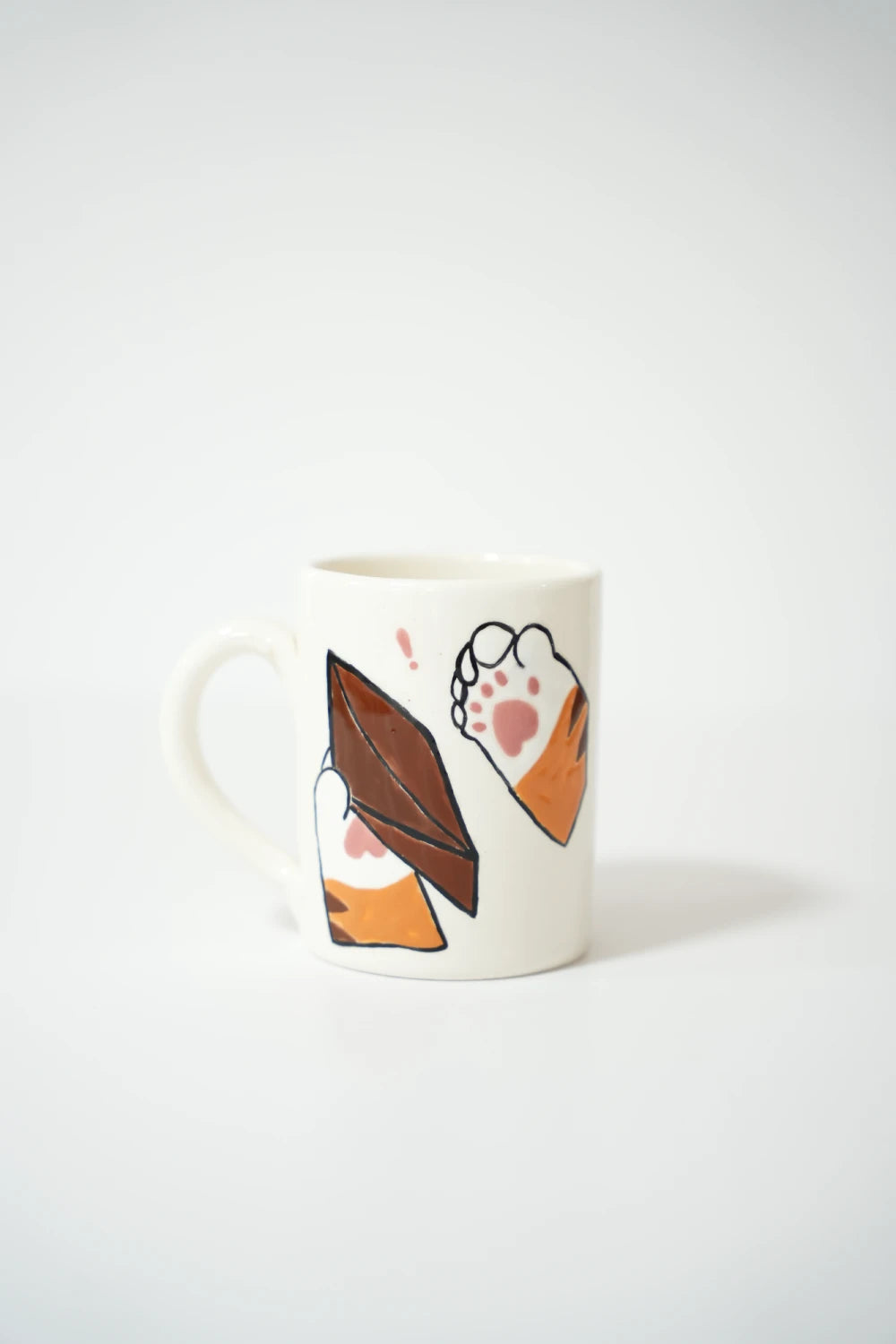 فنجان سيراميك أبيض مرسوم عليه كفّين لقط كرتوني برتقالي مع بصمات كف وردية، يمسك جزدان مصاري بني لونُه واضح أنه فاضي.